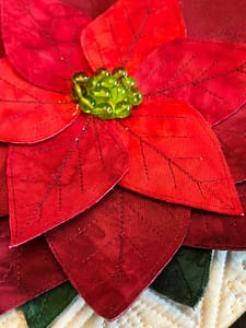 Dimensional poinsettia appliqué by Tourmaline & Thyme Quilts, featuring layered red petals, stitched vein details, and a green beaded center.